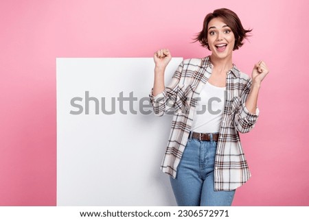 Photo of lucky excited woman dressed plaid shirt rising fists poster empty space isolated pink color background