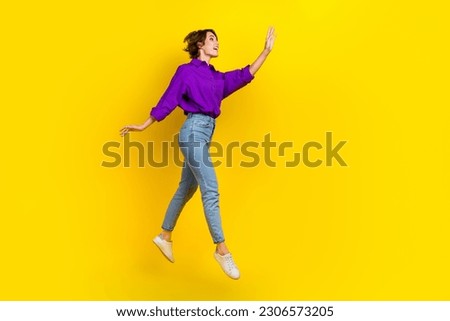 Full length photo of dreamy excited woman dressed purple shirt jumping waving arm empty space isolated yellow color background