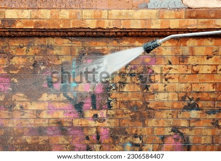 Removal of graffiti paint on a facade. Worker cleaning a dirty brick facade with a pressurized water jet in the integral reform of a house. Municipal facade cleaning service Royalty-Free Stock Photo #2306584407