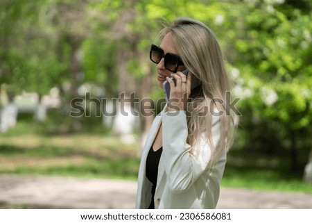 A young blonde woman in sunglasses stands on the street. The girl calls on a mobile phone. High quality photo