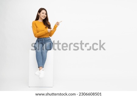 Young Asian woman in yellow shirt sitting and pointing to empty copy space isolated on white background, Full body composition