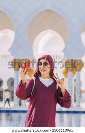 A young tourist girl wearing a traditional Abaya captures her journey through Sheikh Zayed Grand Mosque with a selfie.