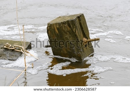 Photo of a square wooden pole that rises diagonally above the water surface, bokeh background.