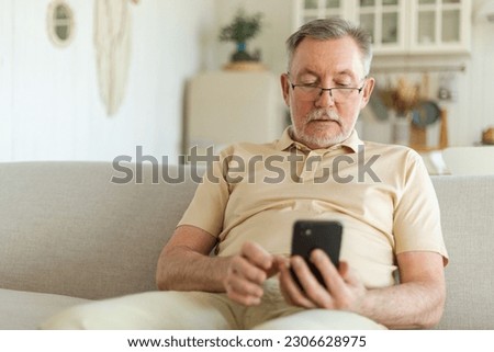 Happy middle aged senior man holding using smartphone touch screen typing scroll page. Stylish older mature beard grandfather with cell phone using internet social media apps at home. Shopping online