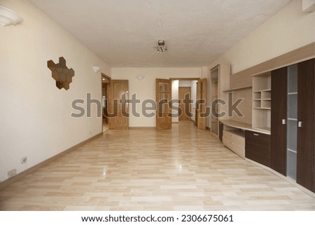 A living room with a wall with some loose furniture, cheap wooden floors, pine wood doors and some mirrors on the wall