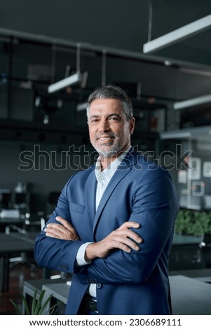 Smiling confident middle aged business man, mature older professional company ceo corporate leader wearing blue suit standing in modern office with arms crossed looking at camera, vertical portrait.