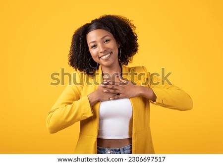 Thank you. Thankful black lady pressing hands to chest and smiling, standing posing over yellow studio background. Gratitude and kindness concept Royalty-Free Stock Photo #2306697517