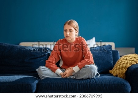 Upset moody teen girl sitting on sofa at home, being sad. Worried depressed adolescent child feeling lonely and frustrated, thinking about problems in school. Teenage mood swings Royalty-Free Stock Photo #2306709995