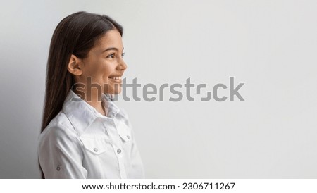 Side View Of Happy Middle Eastern Preteen Girl Standing Looking Aside At Free Space For Text Against White Wall In Studio. Schoolgirl Kid Posing Advertising Your Offer. Panorama Royalty-Free Stock Photo #2306711267