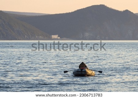 A man in a rubber boat rows with oars. Morning seascape. A fisherman on a boat floats on the sea bay. Mountains in the distance. Fishing and outdoor activities at sea. Magadan region, Far East Russia. Royalty-Free Stock Photo #2306713783