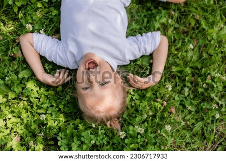 happy little boy lying on the green grass in summer top view in a white turtleneck, space for text. High quality photo