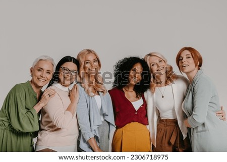 Multi-ethnic group of elegant mature women bonding and smiling against grey background Royalty-Free Stock Photo #2306718975