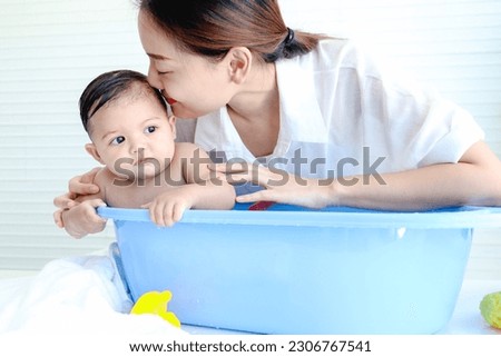 Happy toddle baby infant has fun while taking bubble bath in bathroom, mother bathing kid in tub, mom washing, cleaning and kissing her toddler girl daughter child in bath, childhood and parent care.