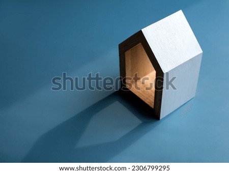 Home, house, family, real estate, property investment concepts. White minimal miniature wooden small house isolated on dark blue background with light and shadow, with copy space.