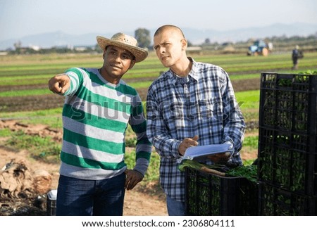 Two males farm workers holding documents talking on farm pointing to something