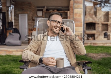 One adult man 40 years old caucasian male sit in front of his house on vacation talk on his smartphone mobile phone call happy smile during the conversation real person copy space Royalty-Free Stock Photo #2306804211