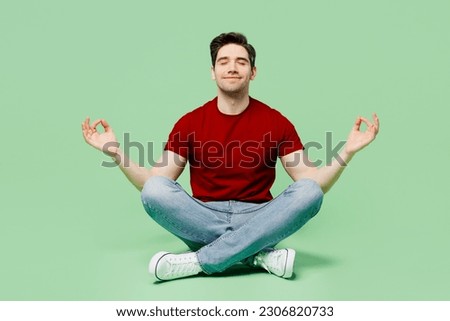 Full body spiritual young man he wearing red t-shirt casual clothes hold spreading hands in yoga om aum gesture relax meditate try to calm down isolated on plain pastel light green background studio