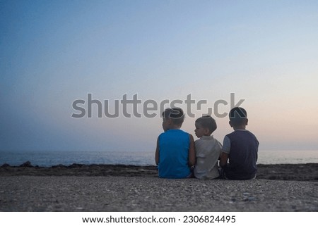 Rear view of children sitting in front of the sea and looking sideways, copy space Royalty-Free Stock Photo #2306824495