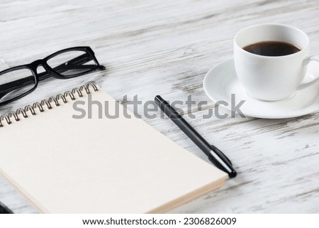Still life of office workspace composition with cup of coffee. Flat lay grunge wooden desk with open spiral notebook, glasses and pen. Coffee break time in cafe. Blank notebook page for notes.