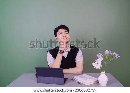 young male worker is at his desk looking for ideas with a smiling expression in front of a green background