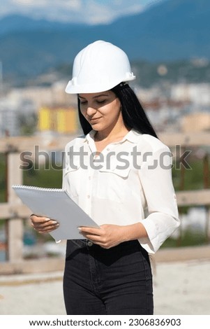 Young female architect in a hard hat on a construction site while working with a paper tablet. Supervisor wearing a protective helmet while working on a construction site. Successful inspector.