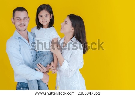 Family portrait father standing holding his cute daughter and a smiling mother standing beside Children hugging happy parents to spend time together with family on a yellow background.