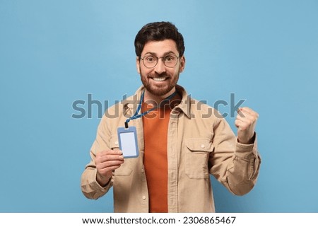 Happy man showing VIP pass badge on light blue background