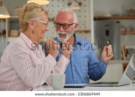 Excited and happy senior couple shopping online from home using computer, smartphone and credit card. Modern technologies and retirement concept.