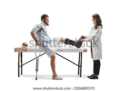 Female doctor putting on a walking brace to a male patient in a hospital gown isolated on white background
