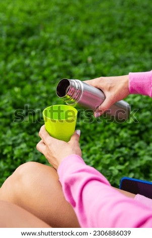 Girl traveler pours tea from a thermos, on the street. Selective focus, noise.  A woman pours a hot drink into a mug from a thermos. High quality vertical photo