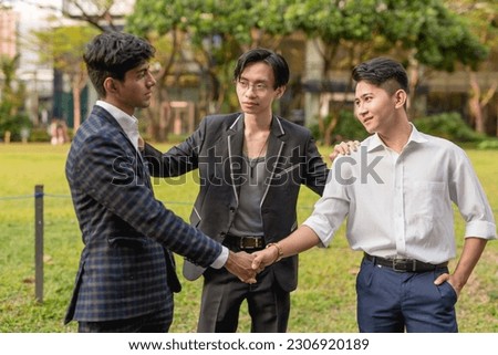 A young asian man gets two former friends and now enemies to shake hands, reconcile and call a truce. A great friend acting as a mediator to patch things up. Royalty-Free Stock Photo #2306920189