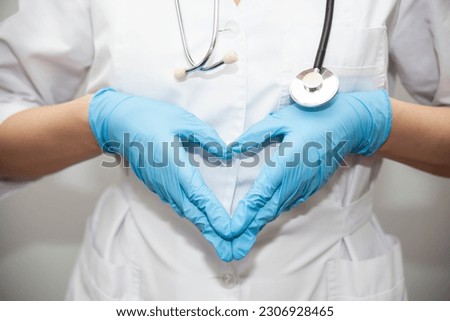 Woman with a medical mask and hands in latex glove shows the symbol of the heart. Doctor for the heart. Love to our pancreas. Love our medical professionals.
