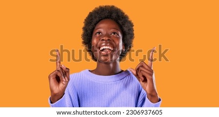 African American young woman with afro hair styling standing in a blue sweater on a bright orange background points up with a thumbs up for an advertising product to insert.