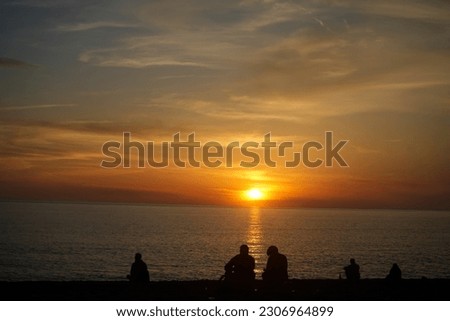 back, rear view of Happy young family or friends sitting near water of Black sea coast. dad, mother and son sit on pebble stone beach. many, a lot person team. blue aqua and sky background. sunset sky
