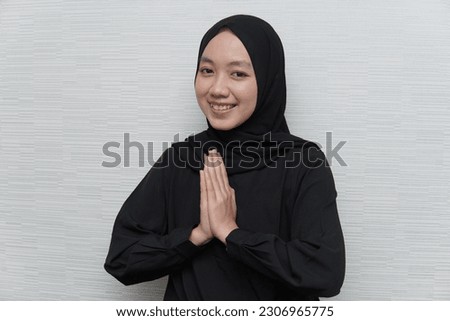 Portrait of a young beautiful Asian Muslim woman wearing a hijab gesturing Eid Mubarak greeting, isolated on white background