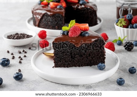 Delicious chocolate cake with chocolate glaze and fresh berries on a white plate on a gray concrete background