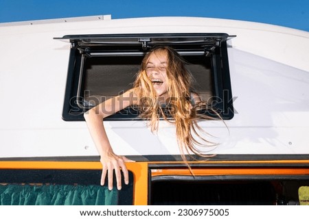 The happy girl sticks her head out of the van window on a wonderful day at camp. Van life concept. Royalty-Free Stock Photo #2306975005