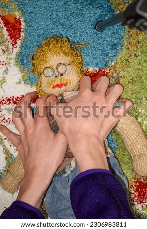 A Gripping Scene: Strangling of a Man Symbol. A Crocheted Male Geek Nerd Engineer Doll with Blond Curls, Mustache, Plaid Shirt, and Glasses! Man strangeled by hands !
