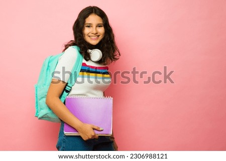 Happy thirteen year old teen carrying a backpack and books while smiling going to junior high school next to pink copy space Royalty-Free Stock Photo #2306988121