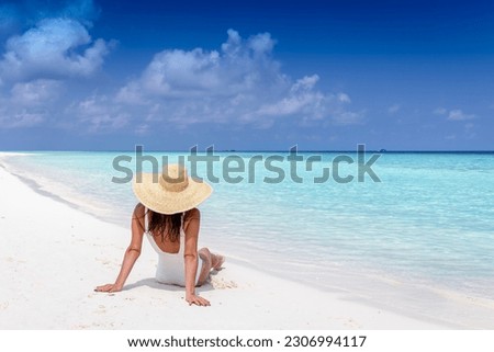 A luxury tourist woman with sunhat sits on a tropical beach and enjoys the sun and turquoise sea Royalty-Free Stock Photo #2306994117