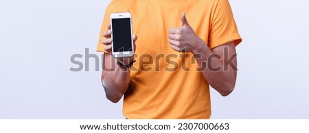 Attractive asian guy in yellow stylish t-shirt with tattoos, showing thumbs-up and smartphone display as offering customer download amazing app, editing application, game or corporate page.