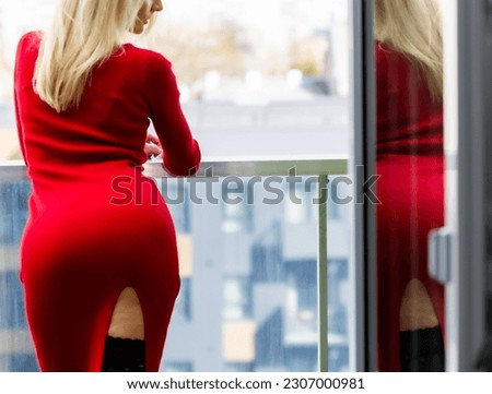 Young beautiful woman in a red dress and high heels on the balcony of an apartment