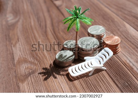 Digital nomads: Stacks of American coins, a toy beach lounger, and a palm tree arranged on a wooden background. Freedom and flexibility of working from a tropical paradise. Royalty-Free Stock Photo #2307002927