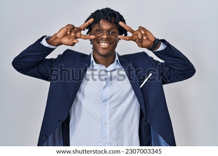 Young african man with dreadlocks wearing business jacket over white background doing peace symbol with fingers over face, smiling cheerful showing victory 