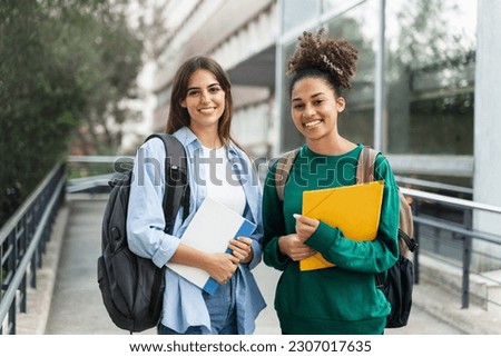Two University Student girls looking at camera smiling outdoors at the college campus . education portrait