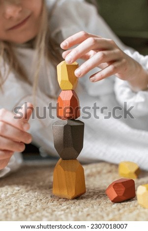 Wooden blocks. 
A girl plays with wooden balancing cubes. Educational games for children. Wooden blocks in shapes of gems of various colours. The girl builds a pyramid from wooden blocks.