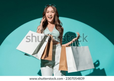 Asian happy female woman girl holds colourful shopping packages   standing on blue background studio shot, Close up Portrait young beautiful attractive girl smiling looking at camera with bags Royalty-Free Stock Photo #2307054839