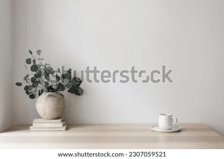 Minimal breakfast still life. Cup of coffee, tea. Empty white wall in sunlight table. Textured vase with silver eucalyptus leaves, branches on old books. Elegant Scandinavian working space, office Royalty-Free Stock Photo #2307059521