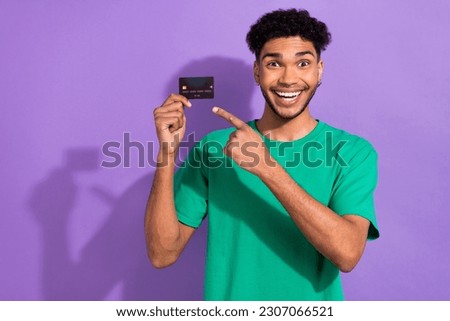 Photo of astonished handsome guy indicate finger debit card wear green t-shirt isolated on violet color background