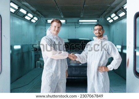 Team of professional automotive painting technician in chemical protecting suit standing in front of the painting chamber together. Car painting and detailing technicians portrait. Royalty-Free Stock Photo #2307067849